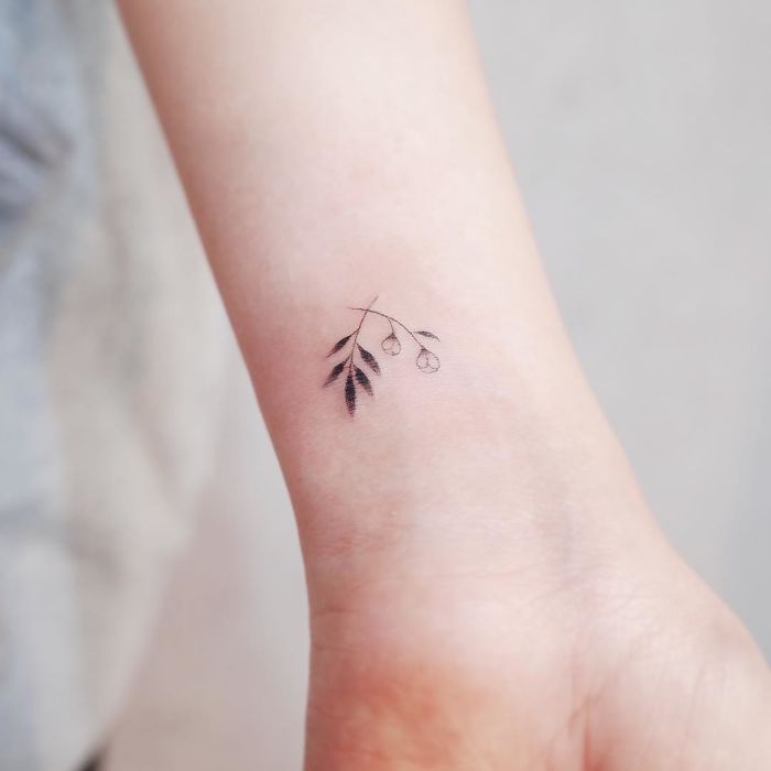 Minimalist tattoo of a delicate branch with leaves on a wrist.