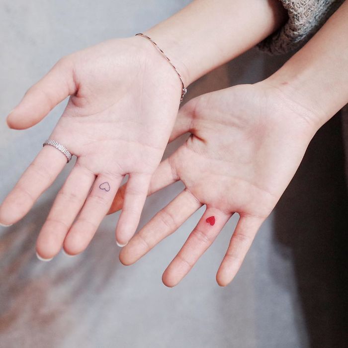 Minimalist tiny heart tattoos on fingers of two hands.