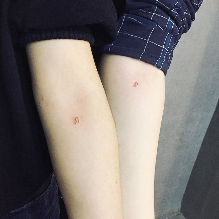 Two minimalism-inspired tiny tattoos of the number 20 on forearms.