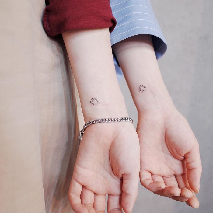 Two minimal heart tattoos on wrists, one wearing a silver bracelet, representing discreet minimalist tattoo style.
