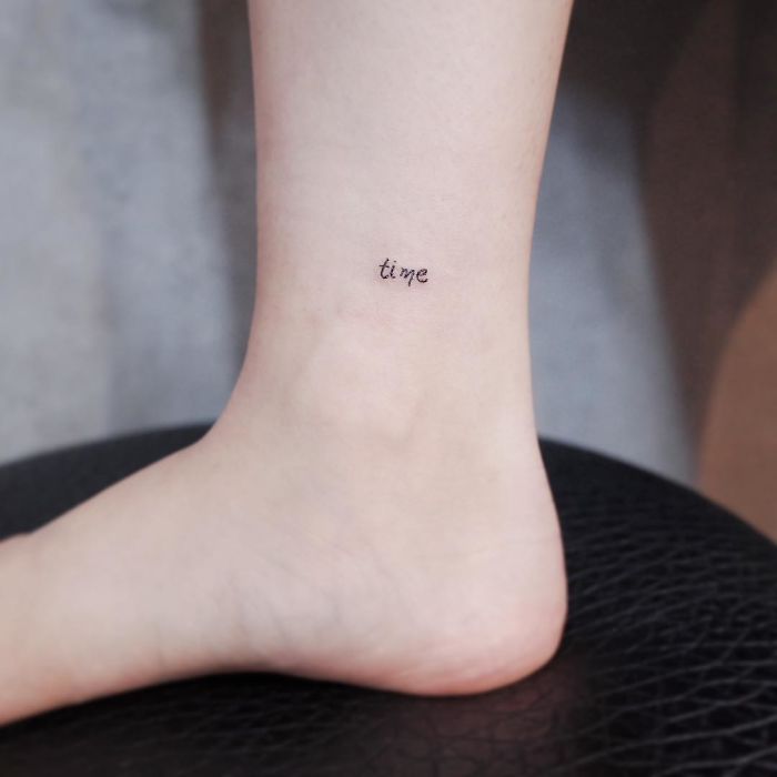 Minimalist tiny tattoo of the word "time" on the lower leg.