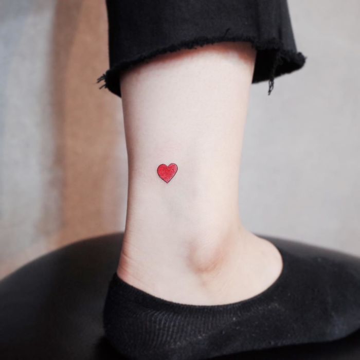 Minimalist tattoo of a small red heart on an ankle, perfect for those who appreciate tiny, discreet designs.