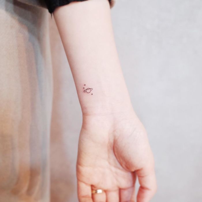 Minimalist tiny tattoo of a small planet on a person's inner wrist.