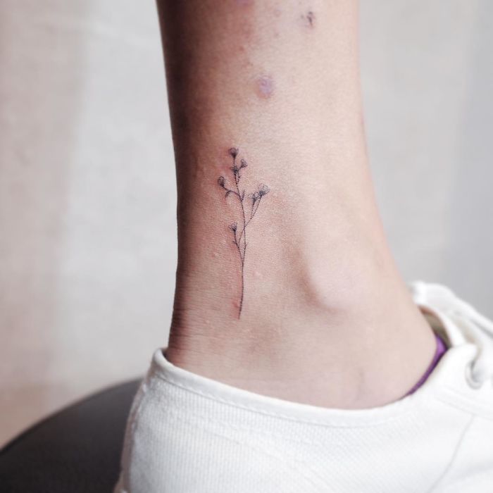 Minimalist tiny tattoo of delicate floral design on ankle.