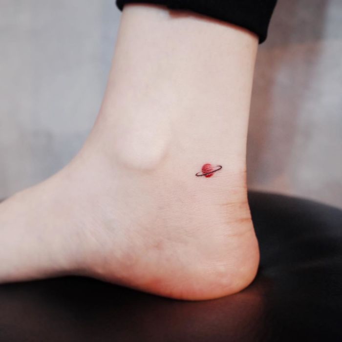 Minimalist tattoo of a red planet with a ring on an ankle, emphasizing tiny discreet designs.