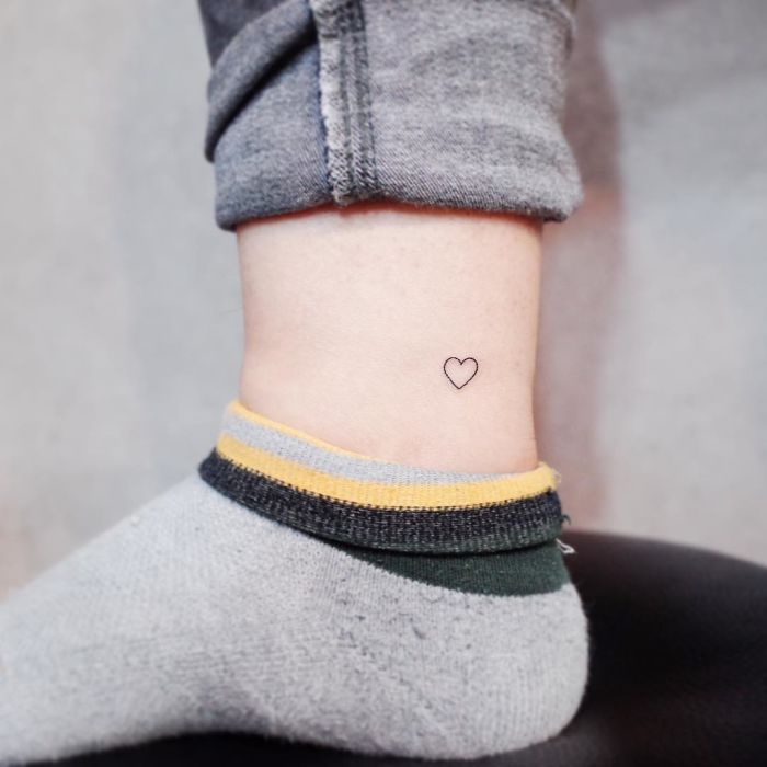 Minimalist tattoo of a tiny heart on an ankle, framed by gray socks.
