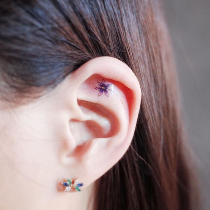 Minimalism tattoo of a tiny flower inside the ear, showcasing discreet design.