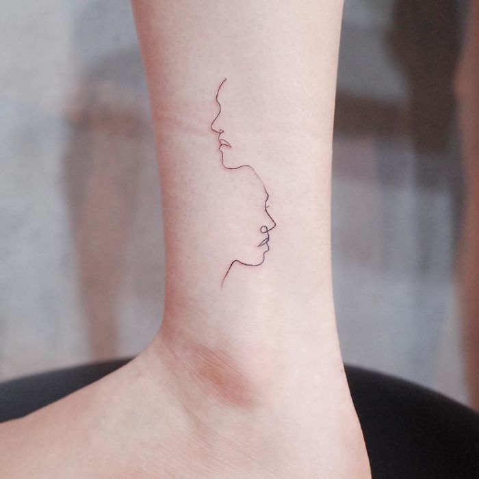 Minimalism tattoo of line art faces on ankle, showcasing discreet tiny tattoo design.