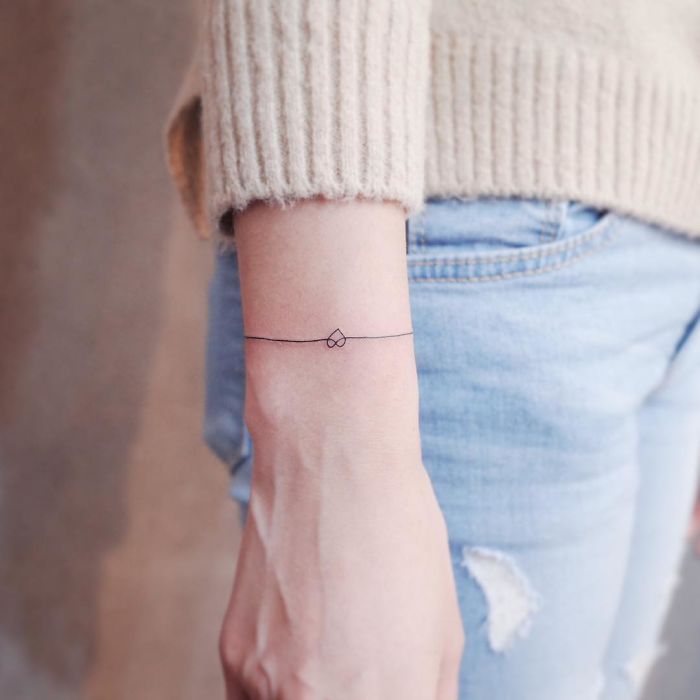 Minimalism tattoo of a heart and line on a person's wrist, showcasing a tiny discreet design.