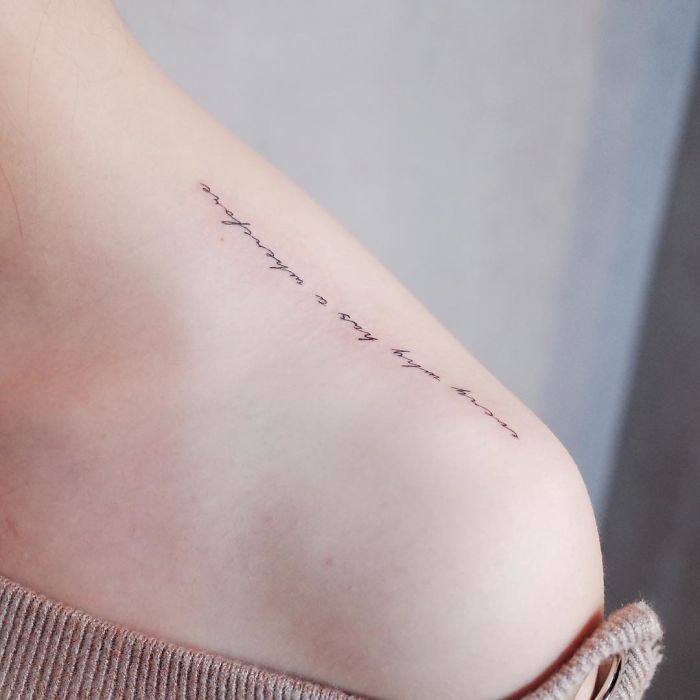 Minimalist script tattoo on shoulder, showcasing tiny discreet ink design.