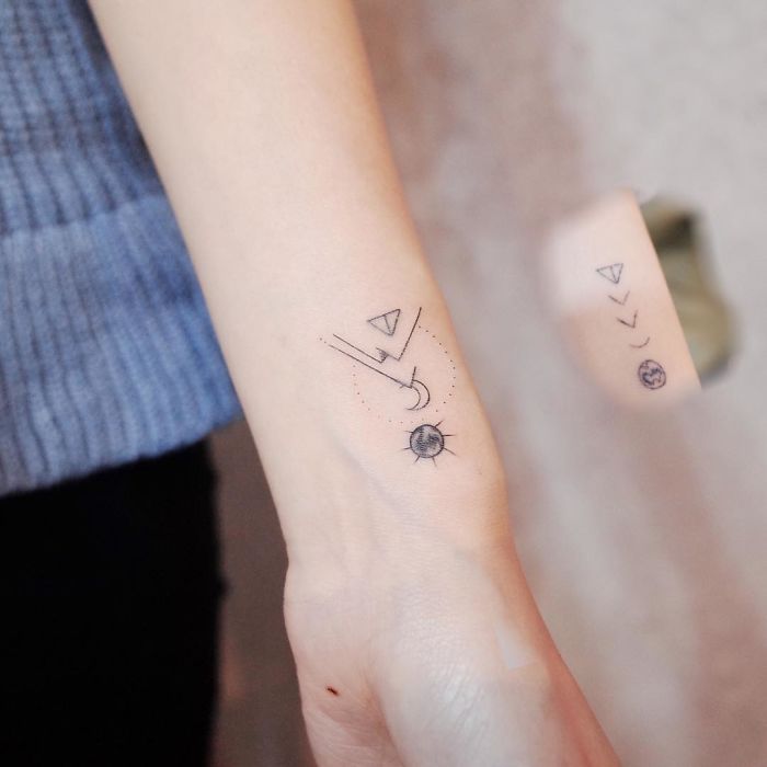 Minimalism tattoo design on a forearm featuring small geometric shapes and celestial symbols.