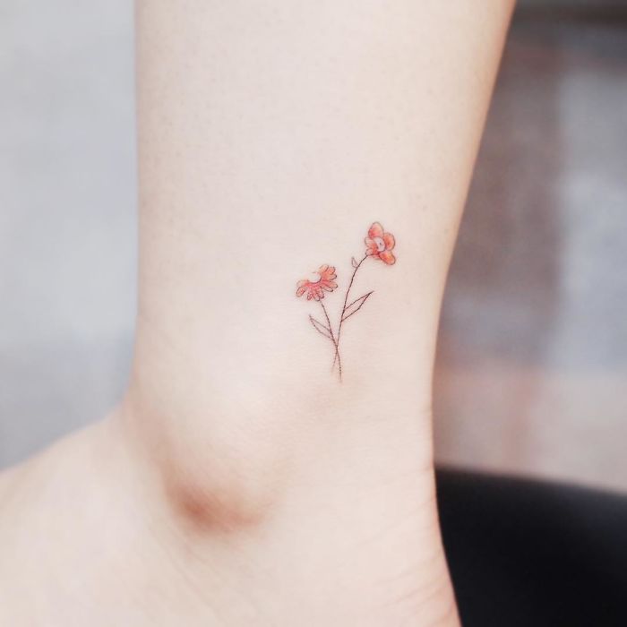 Minimalist tiny tattoo of a delicate red flower on the ankle.