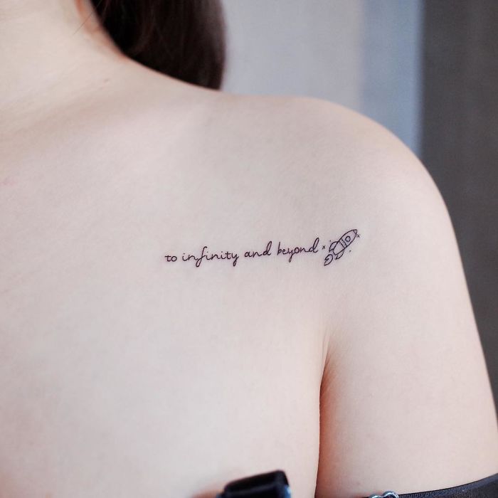 Minimalist tattoo on shoulder with text "to infinity and beyond" and a small rocket illustration.