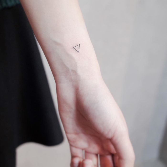Minimalist tiny triangle tattoo on inner wrist, showcasing discreet and elegant body art.