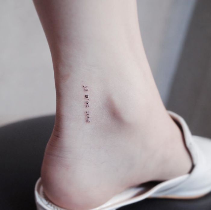 Minimalist tattoo reading "je m'en fous" on the ankle, showcasing a discreet and tiny design.