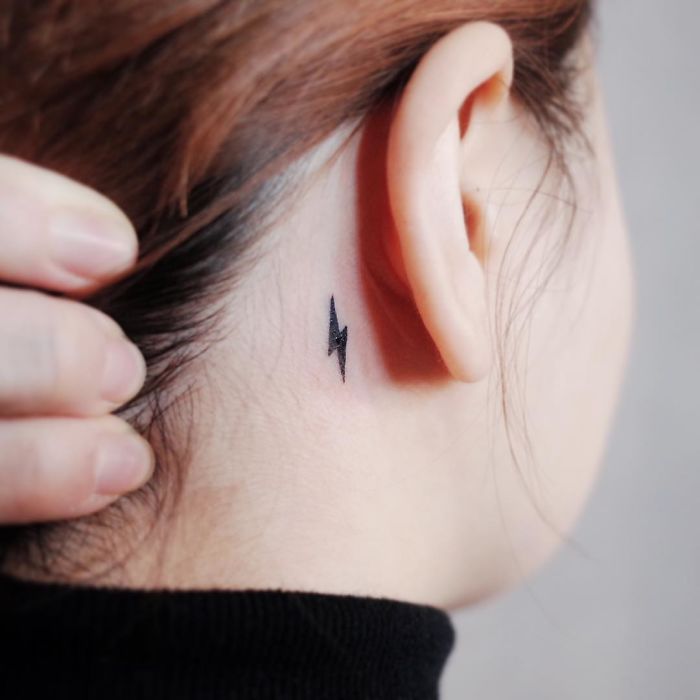 Minimalist tiny lightning bolt tattoo behind the ear.