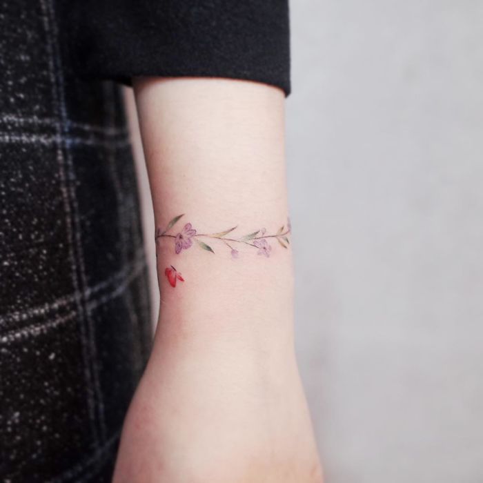 Minimalism-inspired tiny tattoo of delicate purple and red flowers encircling an arm.