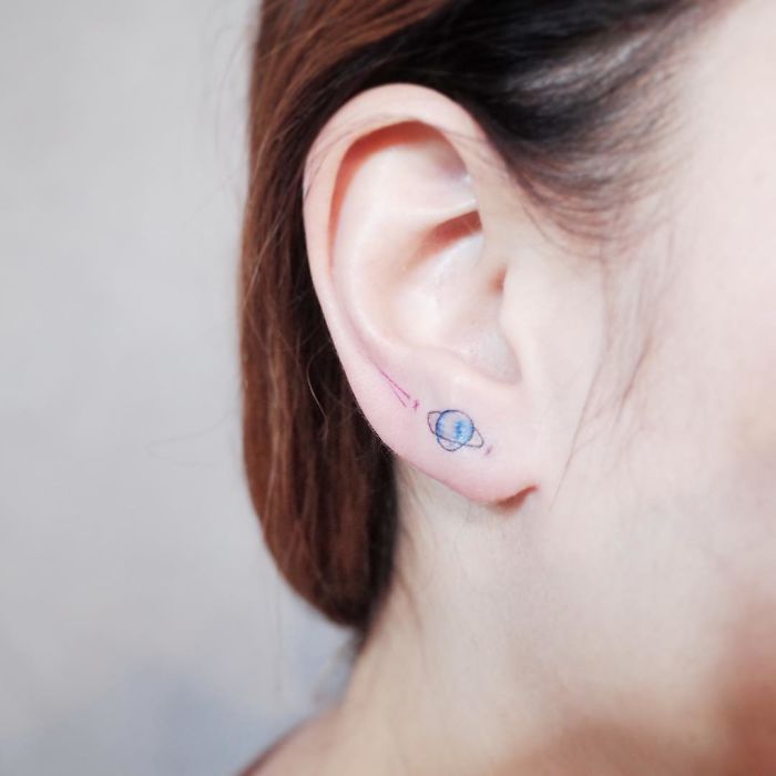 Minimalist tiny planet tattoo on ear, symbolizing discreet tattoo art for minimalism lovers.