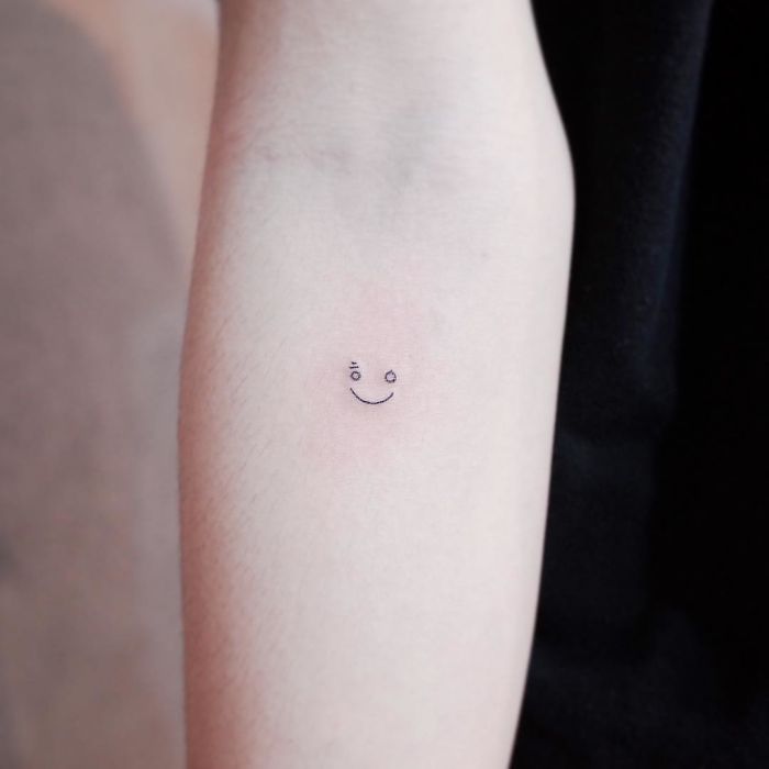 Minimalist tattoo of a tiny smiley face on an arm.