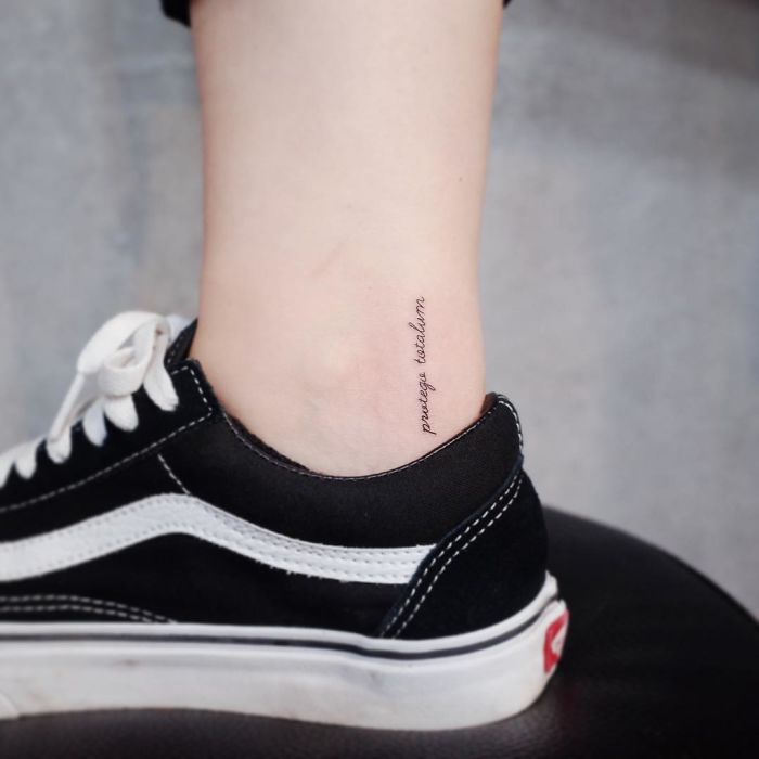 Minimalist tattoo of text on ankle above black sneaker.