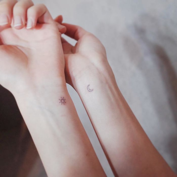 Minimalist tiny tattoos of sun and moon on wrists, showcasing discreet design.