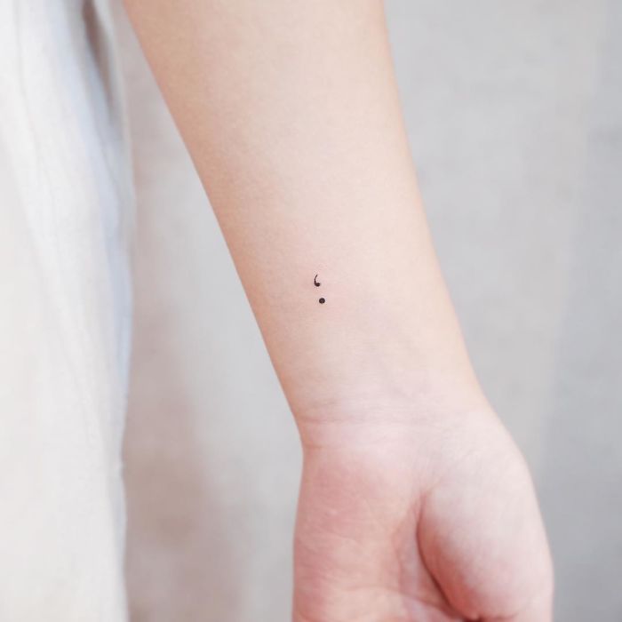 Minimalist tiny semicolon tattoo on inner forearm.