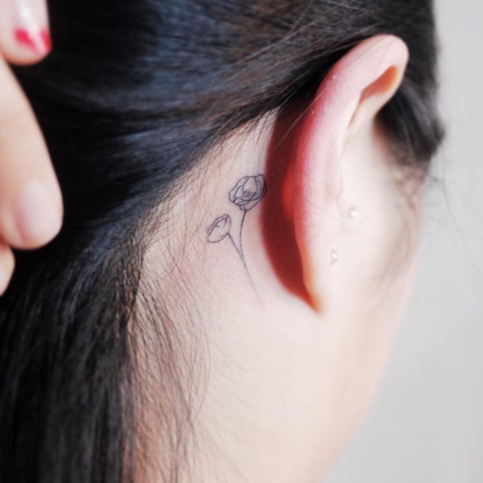 Minimalist flower tattoo behind the ear, emphasizing discreet and tiny designs for those who love subtle body art.