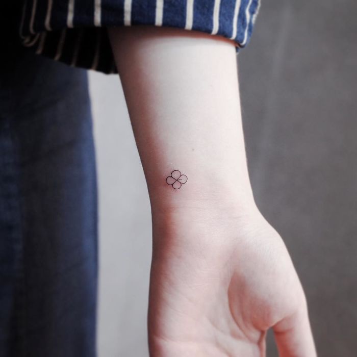 Minimalism tattoo on wrist, featuring a small, simple four-petaled flower design on light skin.