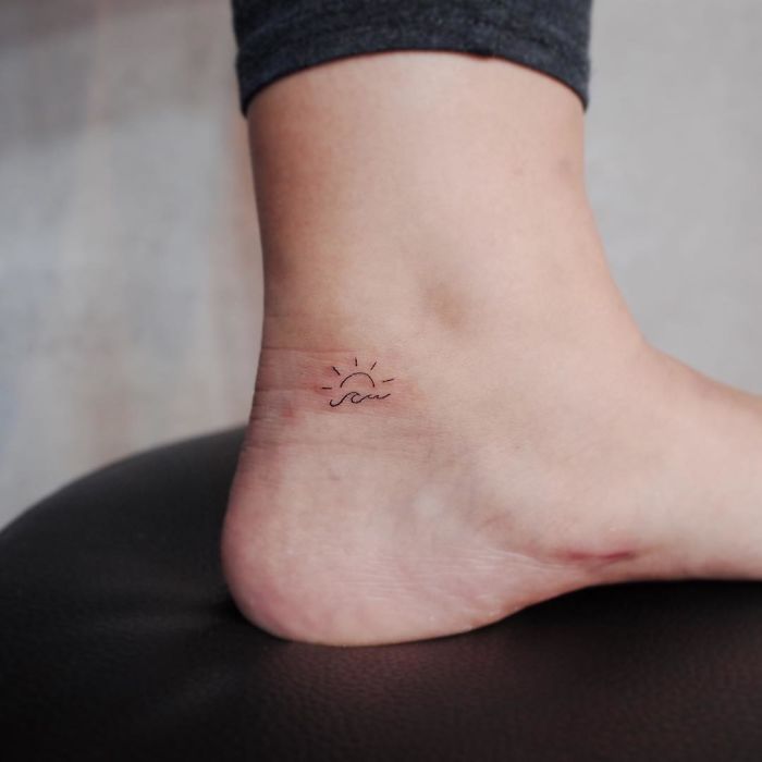 Minimalist tattoo of a sun and wave on an ankle, exemplifying tiny discreet tattoo design.