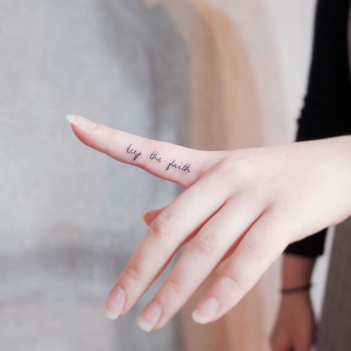 Tiny tattoo on a woman's finger that reads "keep the faith," representing minimalist tattoo design.