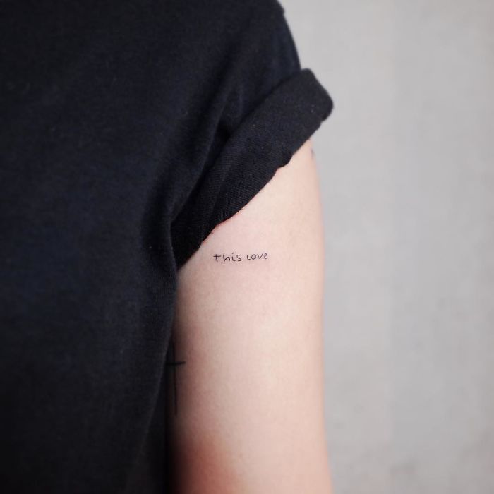 Minimalist tattoo reading "this love" on the upper arm in fine script.