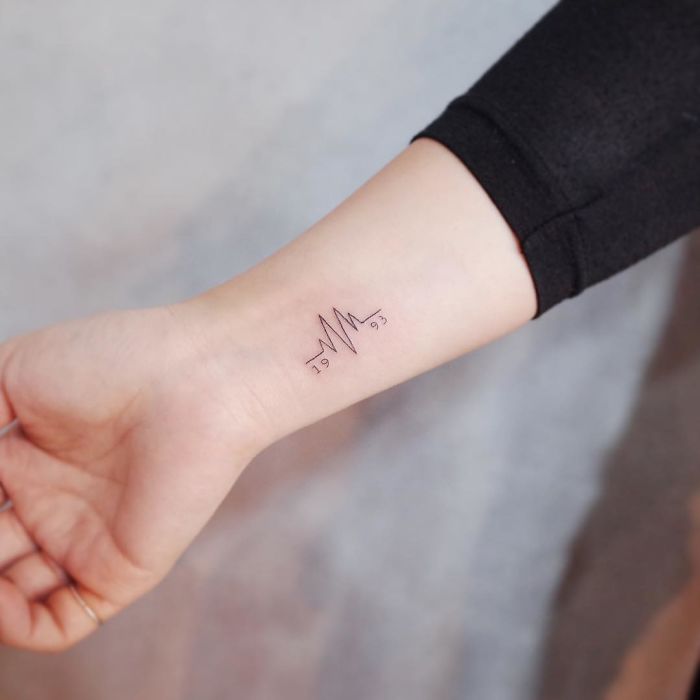 Minimalist discreet tattoo of a heartbeat and numbers on a person's wrist.
