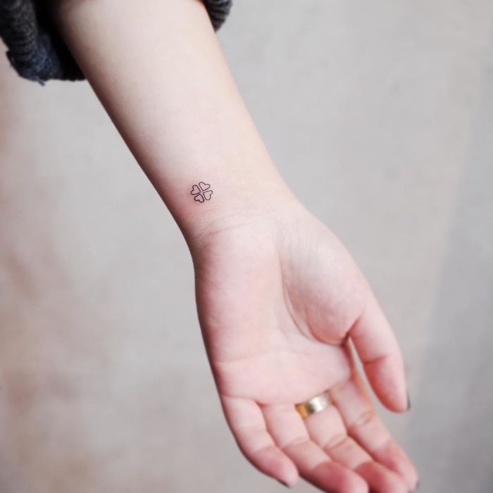 Minimalist small tattoo of a plus sign on a person's wrist.