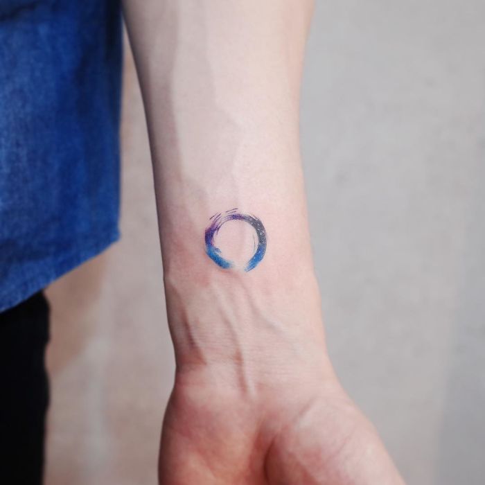 Minimalism tattoo featuring a small colorful circle on a forearm, showcasing discreet design style.