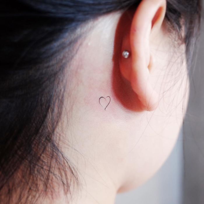 Minimalist tattoo of a tiny heart behind the ear, showcasing discreet body art.