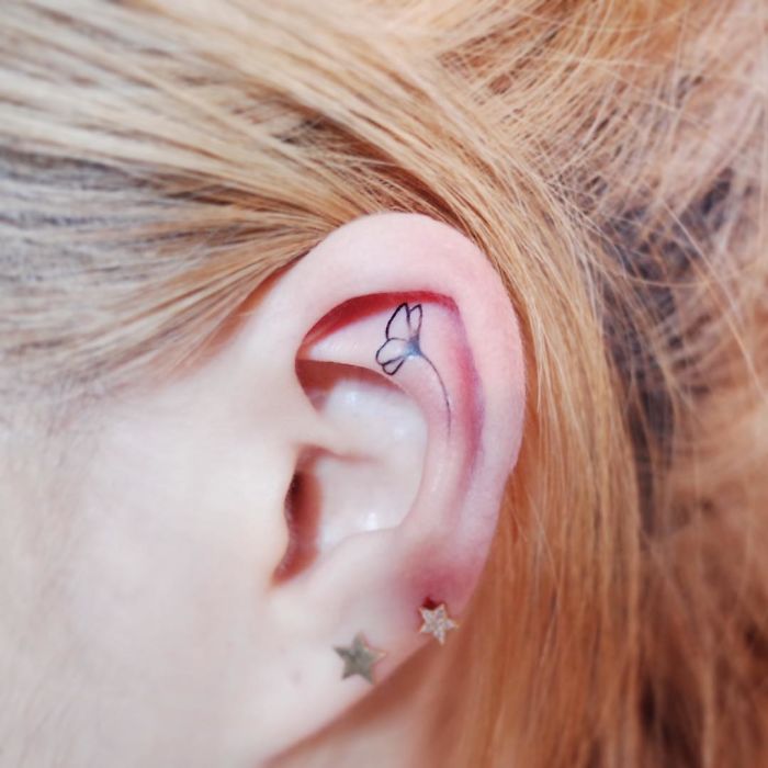 Minimalism tattoo of a small butterfly inside an ear, highlighting discreet design.
