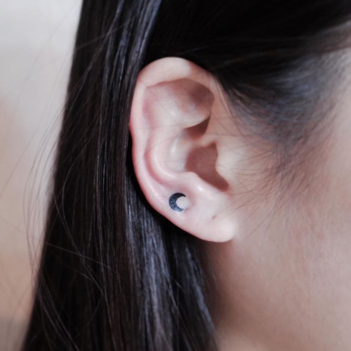 Minimalist tattoo of a crescent moon on woman's ear for tiny discreet tattoo inspiration.