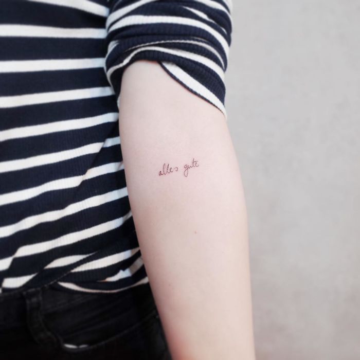 Minimalist tattoo on arm with "alles gute" in cursive, ideal for tiny discreet tattoo lovers.