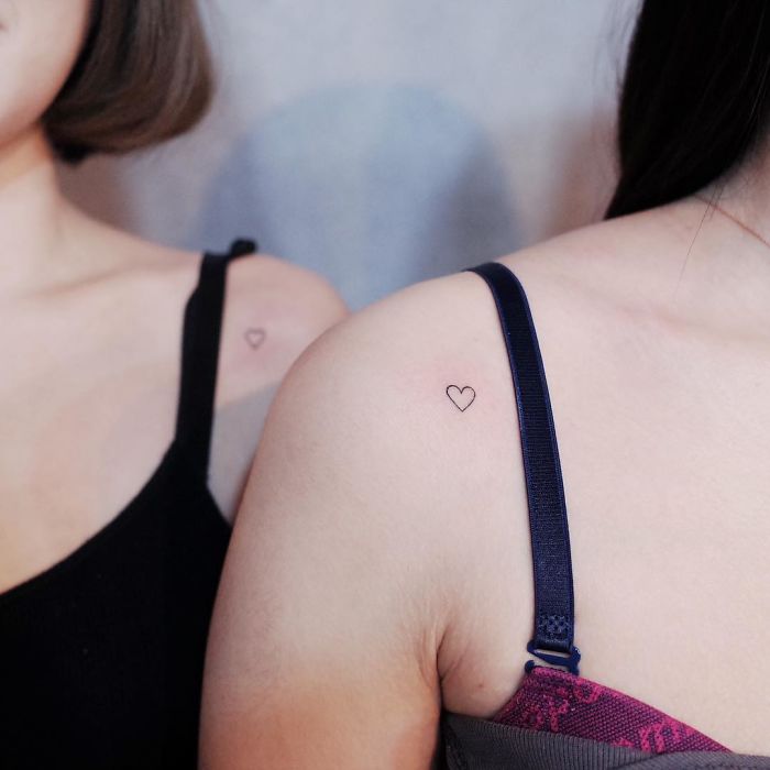 Minimalism tattoos featuring tiny heart designs on two women's shoulders, emphasizing discreet style.