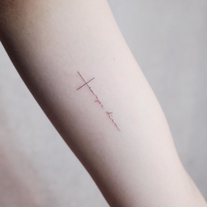 Minimalism tattoo on arm, featuring a delicate cross and line design.