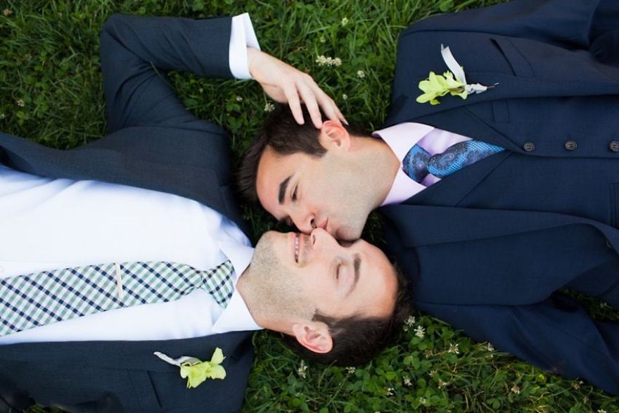 Two men kissing while laying on grass 