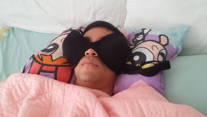 Man using a bra as a sleep mask, lying on cartoon pillows, showing a funny side of being married.