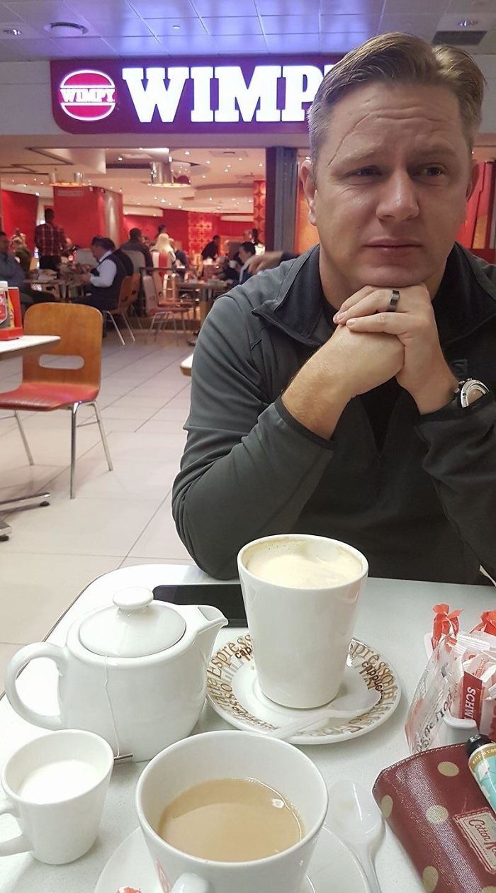 Man with amused expression in a coffee shop, surrounded by drinks, illustrating funny reasons being married is the best.