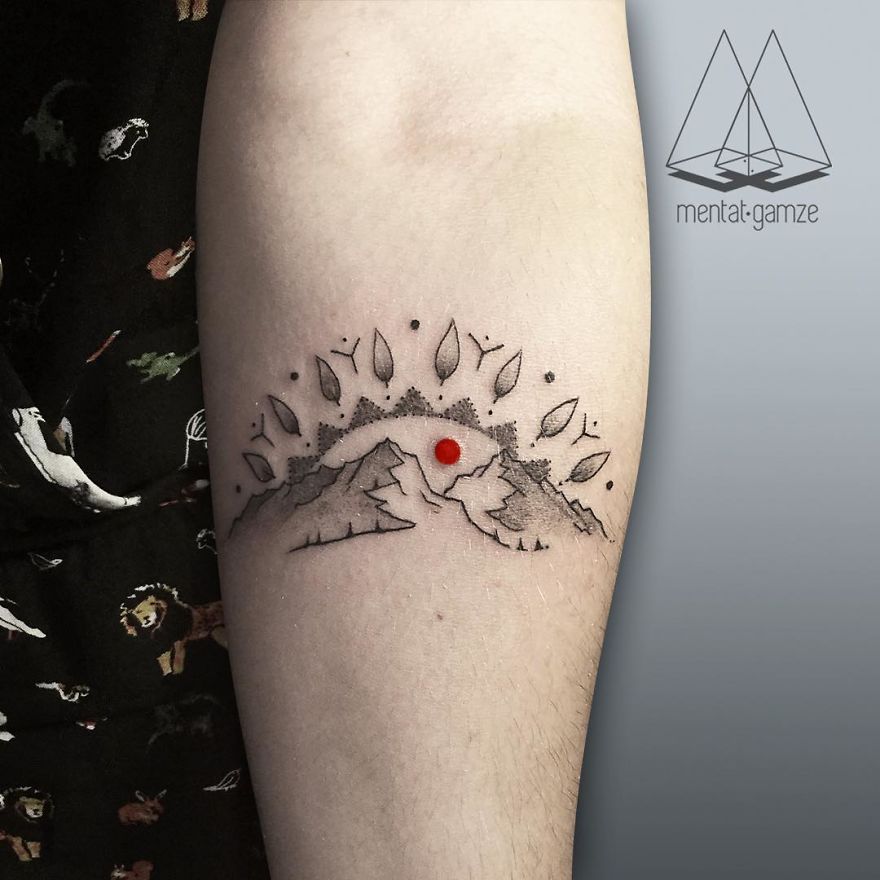 Tattoo of mountains with surrounding patterns and a bright red dot on the forearm, showcasing unique artistry.