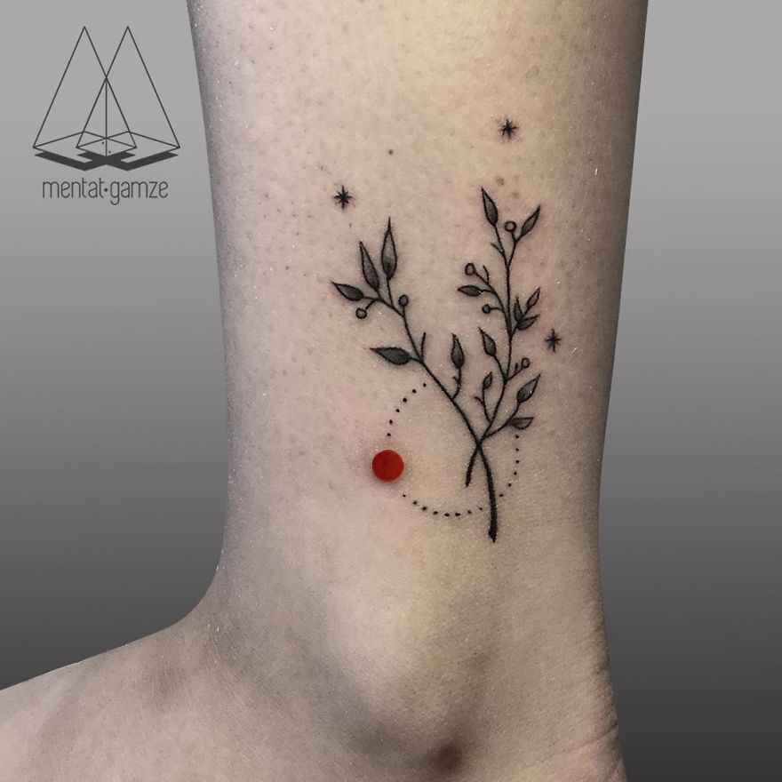 Minimalist tattoo of a branch with leaves, dotted circle, and a red dot on a person's skin.