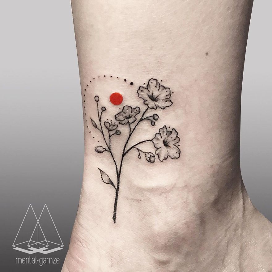 Floral tattoo with black flowers and a red dot on skin, showcasing a creative artist's work.