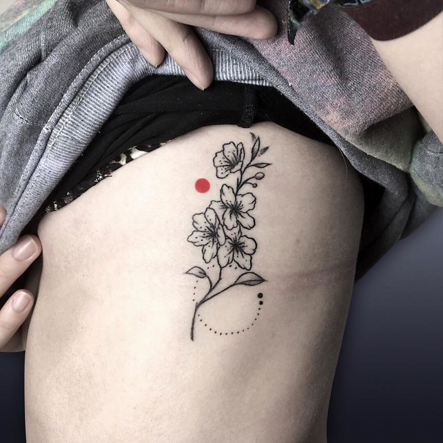 Floral tattoo on side with red dot accent, showcasing new tattoo artist's creativity and technique.