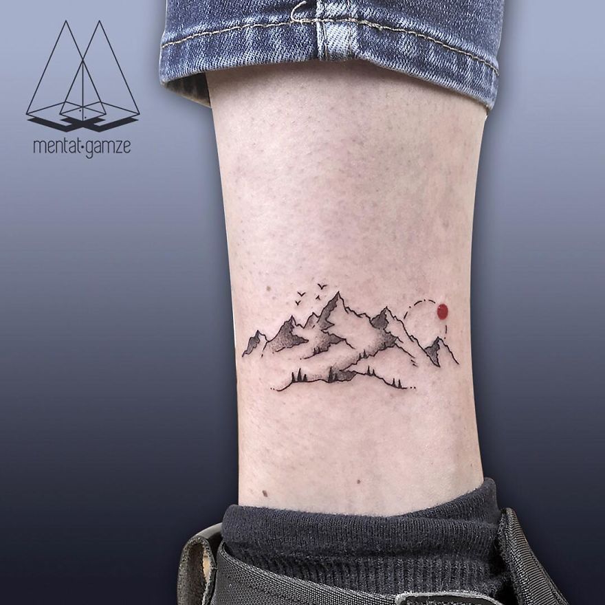 Minimalist tattoo of mountains with a red dot on a person's leg, showcasing tattoo artist creativity.