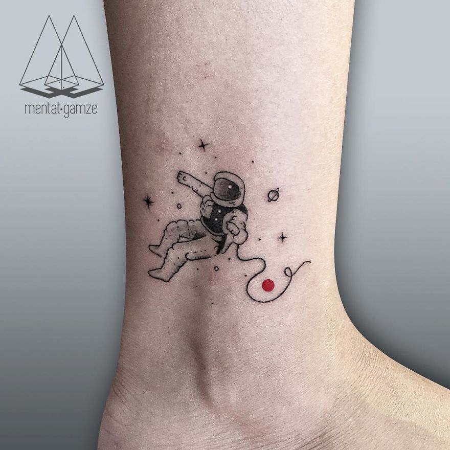 Astronaut tattoo with a red dot, surrounded by stars and planets, on the ankle.