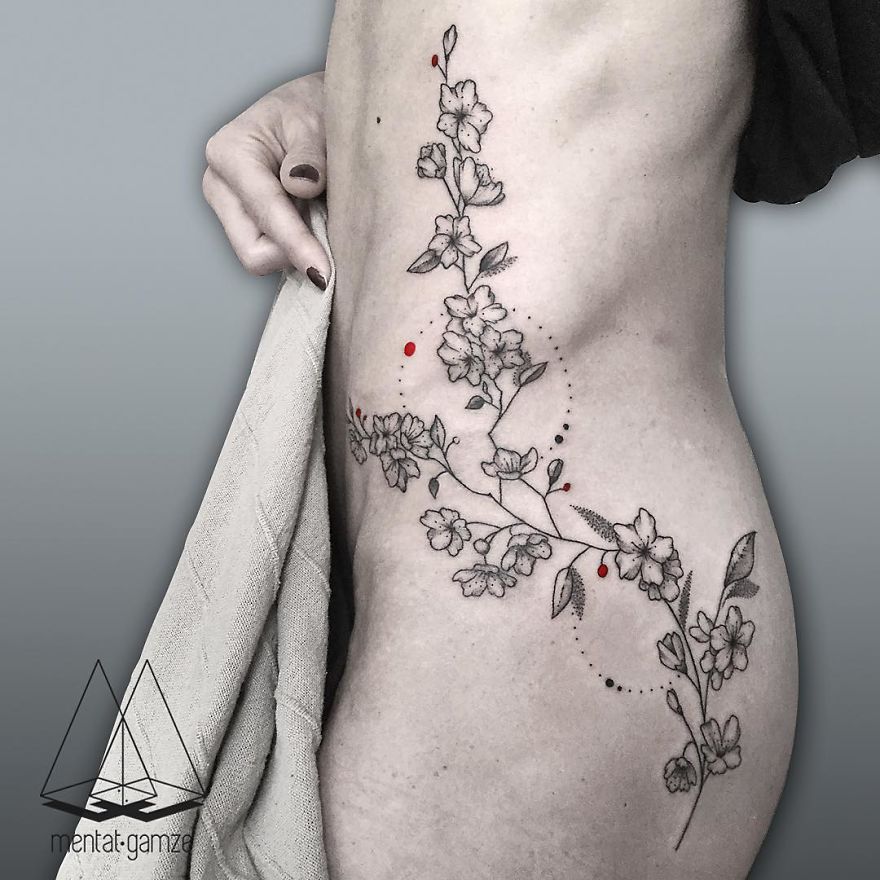 Floral tattoo with red dot on side torso, showcasing tattoo artist's intricate design work.